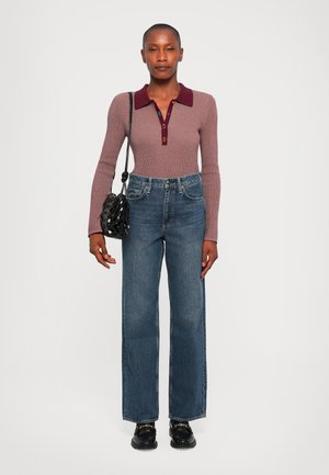 Donna in maglione a coste a maniche lunghe con colletto bordeaux, jeans blue a gamba dritta, borsa nera a tracolla e mocassini neri.
