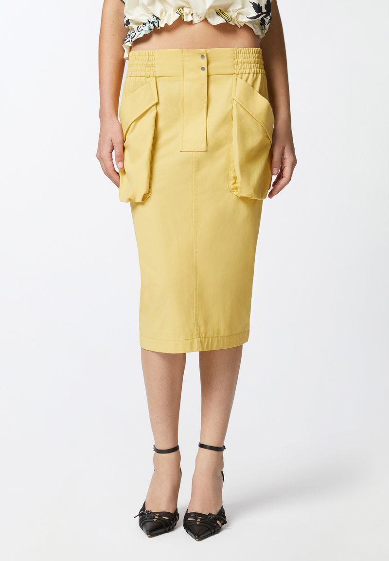 Žuta olovka suknja ima prilagođeni dizajn s bočnim džepovima i gumiranim pojasom. Tkanina je glatka, a suknja je do koljena.