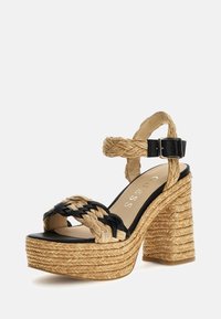 Sandale compensée avec plateforme en jute tressé, lanières en similicuir noir et boucle ajustable à la cheville. Contraste de couleurs naturelles et noires.