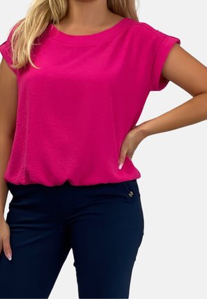 Kortemouws, rondnek top in felroze stof. Zacht, gestructureerd materiaal met een losse pasvorm, gecombineerd met donkerblauwe broek met subtiele hardware.