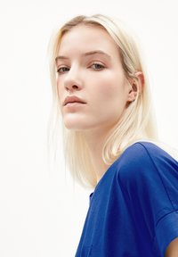 Blauwe katoenen t-shirt met een ontspannen pasvorm, ronde halslijn en korte mouwen. Het model heeft lang, steil, lichtblond haar.