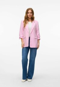 Blazer rosa claro con un ajuste relajado, solapas con muesca y mangas de tres cuartos, combinado con jeans de campana azules y zapatos blancos.