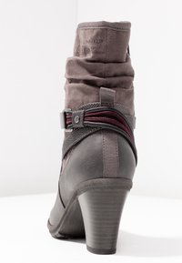 Botín de tacón para mujer en gamuza gris, con un diseño arrugado, una correa decorativa con acentos rojos y un tacón texturizado negro.