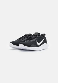 Sorte atletik sko med en struktureret mesh-overdel, fremtrædende hvid swoosh-logo og en hvid sål med grebsmønstre. Snørebåndsdesign.