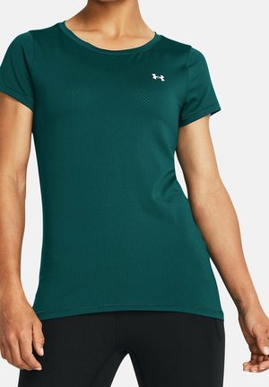 Femme portant un t-shirt de sport à manches courtes vert foncé avec un petit logo blanc Under Armour sur le haut de la poitrine, assorti à un legging noir.