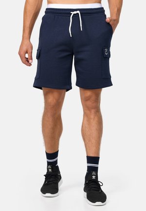 Navy blue cotton blend shorts with elastic waistband, white drawstring, side pockets, and flat stitching. Worn with black sneakers and navy socks.