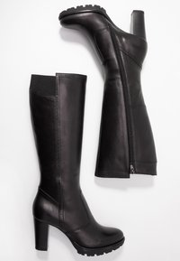 Botas negras de cuero hasta la rodilla con acabado texturizado, tacones altos de bloque y cremallera lateral. Presentan detalles elásticos en la parte superior.