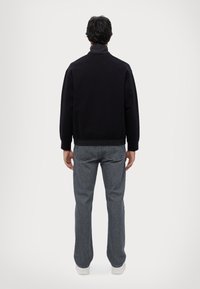 Felpa nera con collo alto, vestibilità rilassata e orlo a coste, abbinata a jeans grigi a gamba dritta e sneakers bianche.