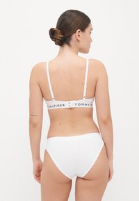 Reggiseno bianco e slip coordinati realizzati in tessuto morbido, caratterizzati da un elastico con la scritta "TOMMY HILFIGER" sulla parte posteriore.