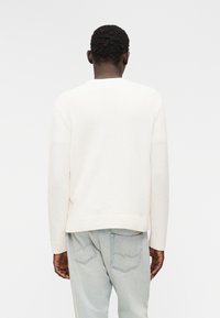 Λευκό πλεκτό πουλόβερ με υφασμάτινη υφή, στρογγυλό λαιμόκοψη και ριμπ τελείωμα, σε συνδυασμό με ανοιχτό μπλε τζιν παντελόνι με πίσω τσέπες.