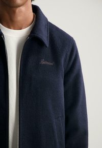 Marine fleece jack met een zachte textuur, voorzien van een ritssluiting en een klassieke kraag. Subtiele logo in lichte draad op de borst.