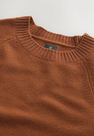 Sweter w kolorze rdzy z dzianiny, z prążkowanym okrągłym dekoltem. Oferuje teksturowany materiał oraz subtelne detale przeszycia wzdłuż ramion.