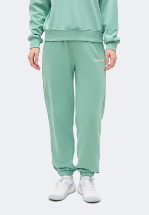 Άτομο που φοράει αθλητική φόρμα Björn Borg σε μέντα πράσινο χρώμα και ταιριαστό φούτερ, σε συνδυασμό με λευκά αθλητικά παπούτσια.