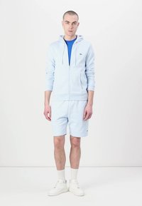 Svetlo modrá mikina na zips s klokankou, zodpovedajúce šortky a modré tričko. Biele tenisky a ponožky po členky dopĺňajú outfit.