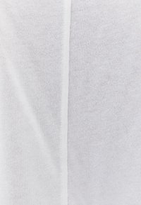 Tessuto bianco lavorato a maglia con una cucitura verticale al centro, che mostra punti fini e uniformi e una texture liscia.