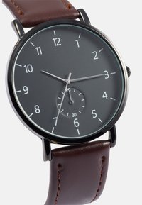 Brown leather strap watch with a black dial, white hour markers, and silver hands. Includes a small subdial at six o'clock.