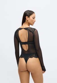 Črno bodi z prosojnimi dolgimi rokavi, čipkastimi poudarki na ramenih in hrbtu ter odprtino v obliki kapljice. Eleganten, oprijemal dizajn.