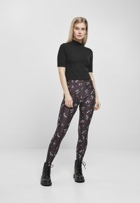 Haut noir à manches courtes associé à des leggings à motifs arborant des designs floraux multicolores sur un fond sombre, complété par des bottes noires.