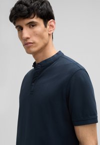 Polo bleu marine avec un col structuré, patte de boutonnage à trois boutons et manches courtes. Tissu en coton lisse avec une texture subtile.
