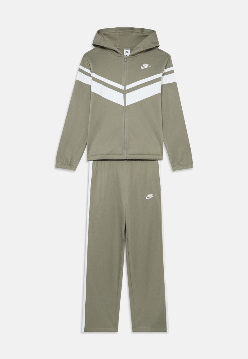 Olive zaļš Nike treniņtērps, ar rāvējslēdzēju un baltiem chevron svītriņām. Komplektā ietilpst kapuce un izšuvums uz krūtīm un augšstilba.