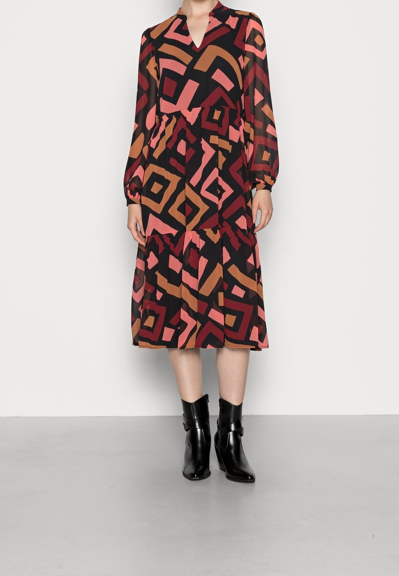 Robe midi à manches longues avec motif géométrique abstrait en noir, rouge, rose et marron, accompagnée de bottines noires.
