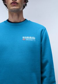 Blauwe sweatshirt met een ronde hals en ribbelboorden. Voorzien van een wit geborduurd logo op de borst, een gladde textuur en een casual pasvorm.