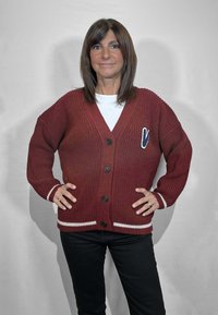 Cardigan marrone lavorato a maglia con scollo a V, cinque bottoni neri e dettagli a righe bianche su polsini e orlo. Abbinato a pantaloni neri.
