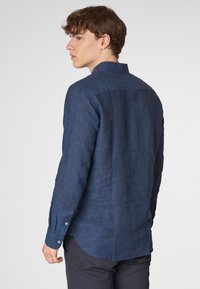 Camicia di lino blu navy con maniche lunghe e polsini abbottonati. Il tessuto ha una finitura texture e un orlo curvato.