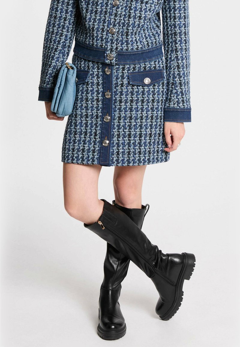 Vestido de tweed con estampado azul y acentos de denim, con botones en el frente y dos bolsillos laterales; combinado con botas de piel negra hasta la rodilla con suelas texturizadas.