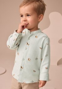 Camisa abotonada de color verde menta claro con estampados de animales, mangas largas y cuello mandarín. Tela suave y corte recto clásico.