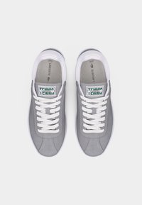 Pár sivých tenisiek Lacoste s bielymi šnúrkami, bielymi podrážkami a zeleno-bielymi značkovými štítkami na jazyku, zobrazených zhora.