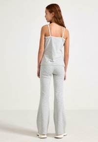 Szary bawełniany top na ramiączkach z cienkimi paskami i jasnoróżowymi akcentami, w zestawieniu z szarymi rozszerzanymi spodniami. Gładka tekstura, luźny krój.