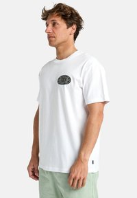 Hvid bomulds t-shirt med et rundt, broderet grafisk motiv i mørke og lysegrøn på venstre bryst. Korte ærmer og rund halsudskæring.