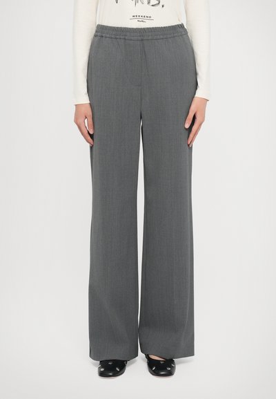 Pantaloni a gamba larga grigi realizzati in tessuto testurizzato con cintura elastica. Abbinati a una camicia bianca a maniche lunghe e scarpe nere.