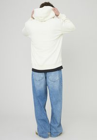 Un sweat à capuche blanc, à coupe ample et à ourlet côtelé, associé à un jean baggy bleu clair, doté de poches arrière et d'une texture délavée.