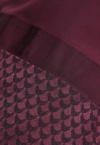 Haut bourgogne avec un tissu lisse et brillant sur le dessus et une section inférieure texturée et à motifs, avec des formes sombres répétées.