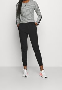Maglietta grigia a maniche lunghe in tessuto testurizzato con dettagli neri, abbinata a pantaloni sportivi neri affusolati e sneakers bianche con dettagli rosa.