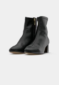 Une paire de bottines en cuir noir avec des talons blocs et des zippers dorés sur le côté, présentées sur un fond blanc.