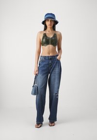 Grøn cropped bralette med lynlås, forvaskede blå denim jeans, blå bøttehat med frynsede kanter og lille blå håndtaske.