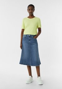 Jasnozielony t-shirt z krótkim rękawem w połączeniu z ciemnoniebieską, dżinsową spódnicą w kształcie litery A. Spódnica ma średnio wysoką talię oraz kieszenie z przodu. Białe trampki uzupełniają całość.