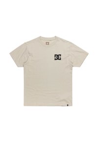 Hellbeige Baumwoll-T-Shirt mit Rundhalsausschnitt, kurzen Ärmeln und einem kleinen schwarzen DC-Logo auf der linken Brust. Einfaches Design, glatte Textur.