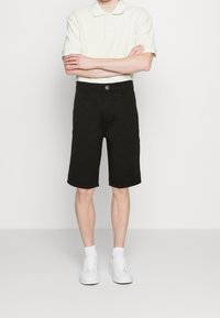 Černé bavlněné šortky se střihem rovného střihu, s knoflíkovým zapínáním a bočními kapsami. V kombinaci se světlým polo tričkem a bílými teniskami.