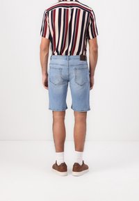 Man standing facing away, wearing light blue denim shorts, a short-sleeve vertically striped shirt, white socks, and brown sneakers.