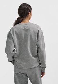 Grauer Pullover mit lockerer Passform, ausgestattet mit Rundhalsausschnitt und tief sitzenden Schultern. "F.U.T." auf der Rückseite bedruckt. Weicher, strukturierter Stoff.