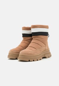 Botas aislantes marrones con parte superior acolchada, detalles de ante, bandas de acento en negro y blanco, y una suela de goma gruesa con tracción.