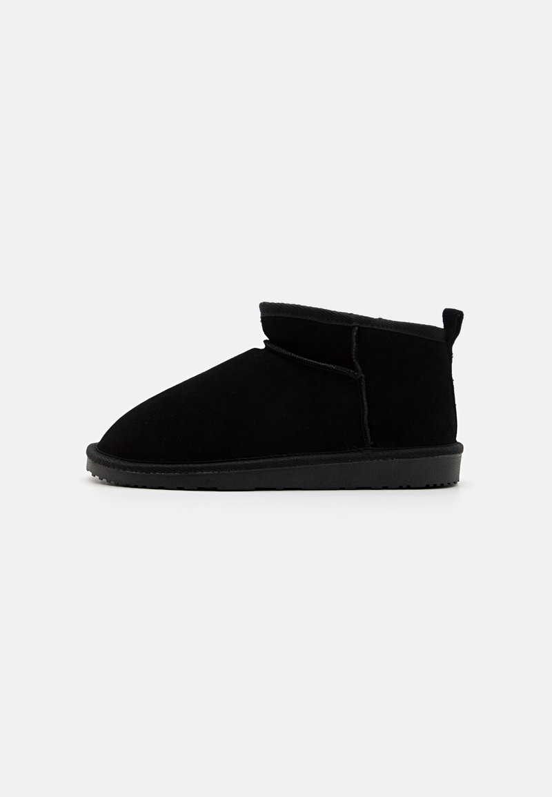 Botas de tobillo de ante negro con punta redondeada, forro suave y caña corta. Presentan una lengüeta en la parte posterior y una suela de goma texturizada.