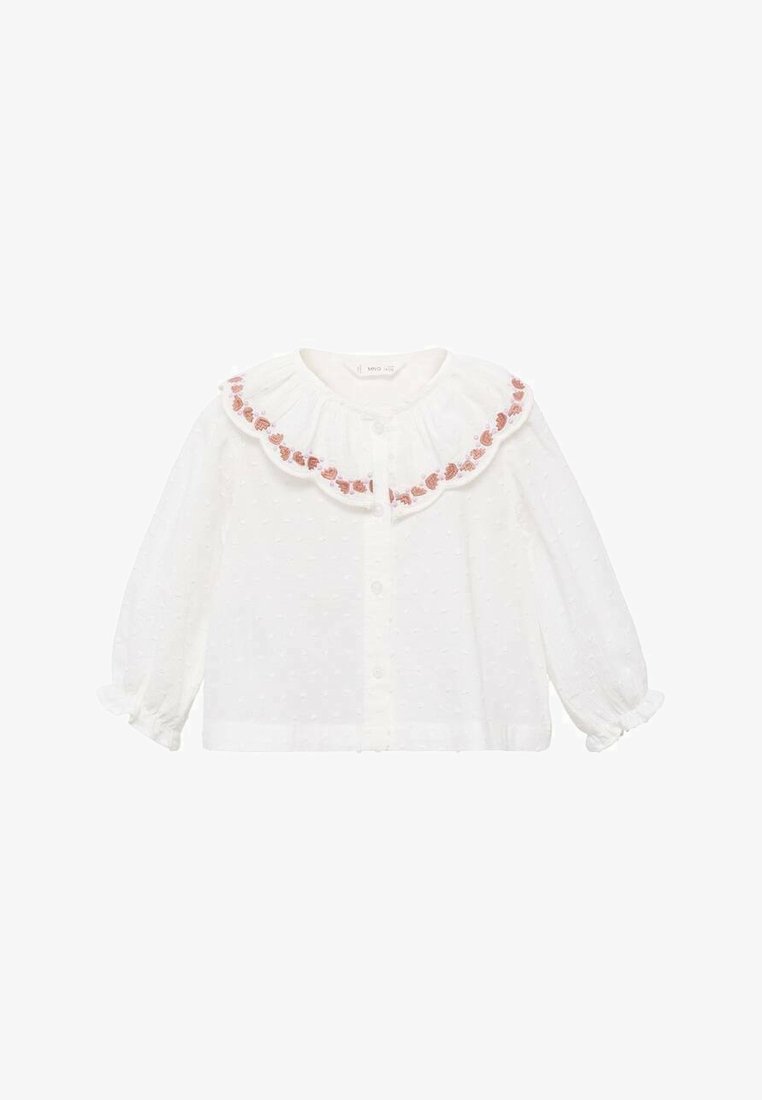 Camisetta bianca con colletto arricciato, decorata con ricami floreali rosa. Maniche lunghe con polsini elastici e texture a pois su tutta la superficie.