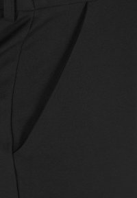 Primo piano di un tessuto nero con una texture liscia, caratterizzato da un dettaglio di cucitura diagonale e una piega per dare forma. Nessun motivo o accessorio visibile.