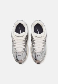 Paire de chaussures de course Nike Air Pegasus argentées et blanches vues de dessus avec des lacets blancs et des semelles intérieures noires avec le logo Nike.