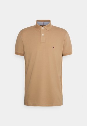 Beiges Polohemd mit kurzen Ärmeln, zwei weißen Knöpfen, Kragen und kleinem rechteckigem Logo auf der linken Brust.